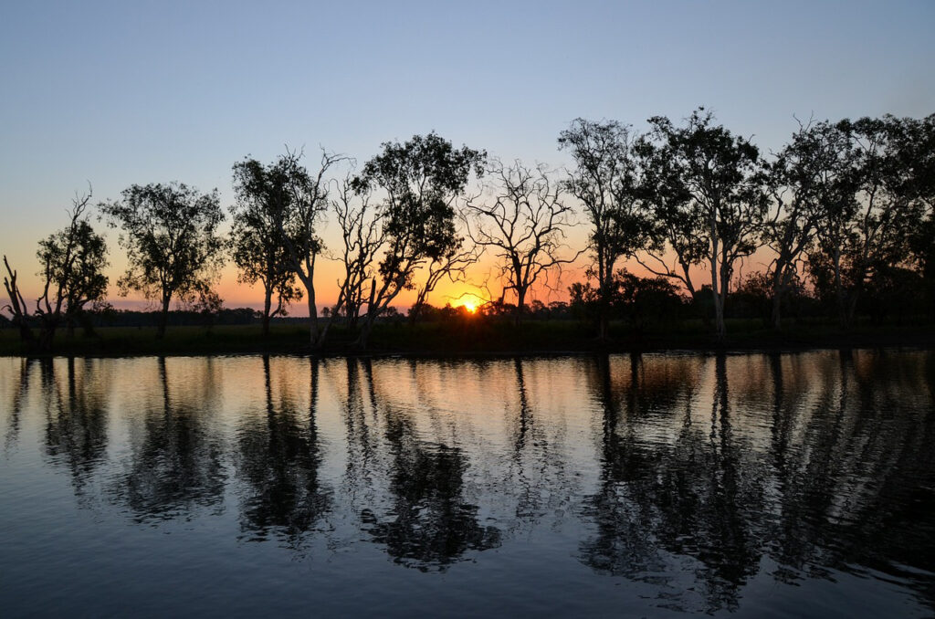 Yellow Water Billabong at sunset. Silhouetted trees are reflected in the waters as the sunsets behind them.