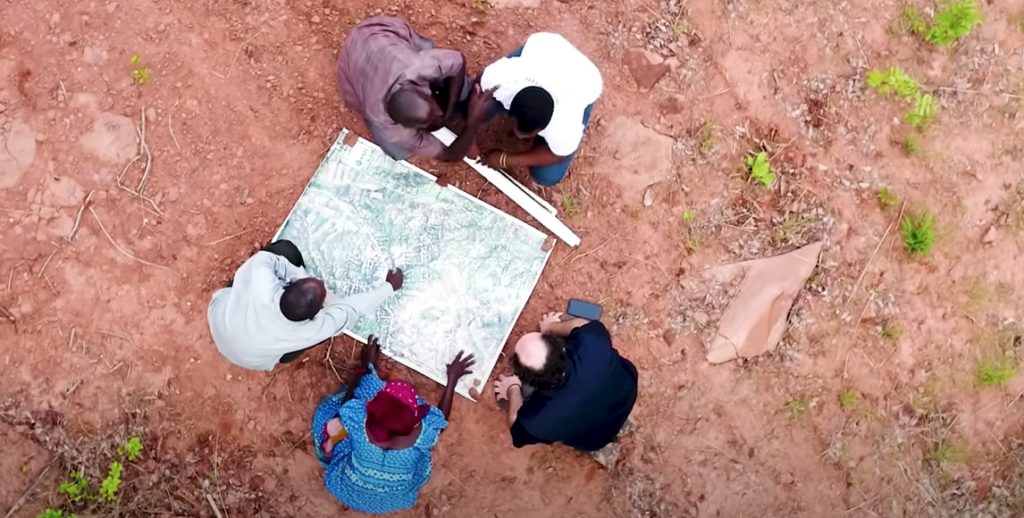 An aerial photo of five people gathered around a large satellite image in the field.
