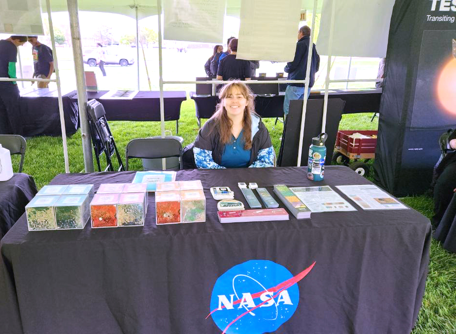 Allison Nussbaum sits at the Landsat table at Maryland Day on the University of Maryland, College Park campus. The change-over-time activity cubes can be seen on the left.