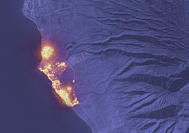 A night scene shows a bright orange patch near the coast burning the city of Lahaina. The rest of the land looks purple in this night image.