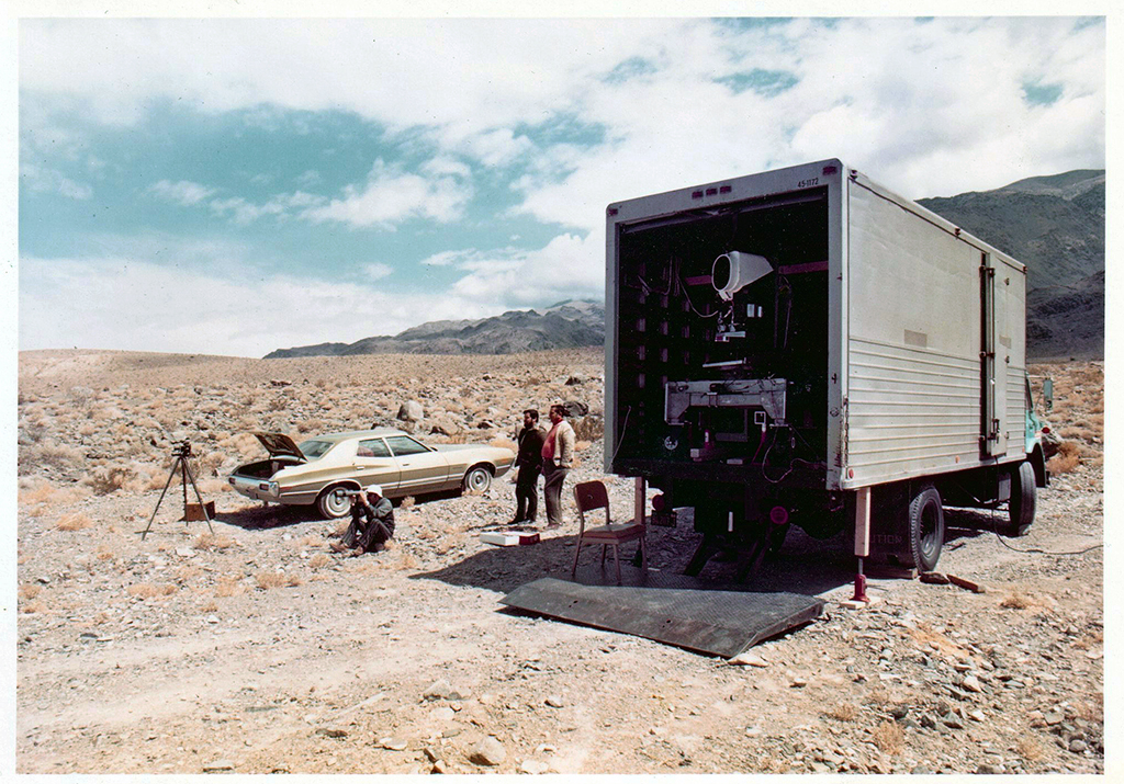 The Landsat 1 MSS engineering model on the back of a truck with three people, and a car in background.