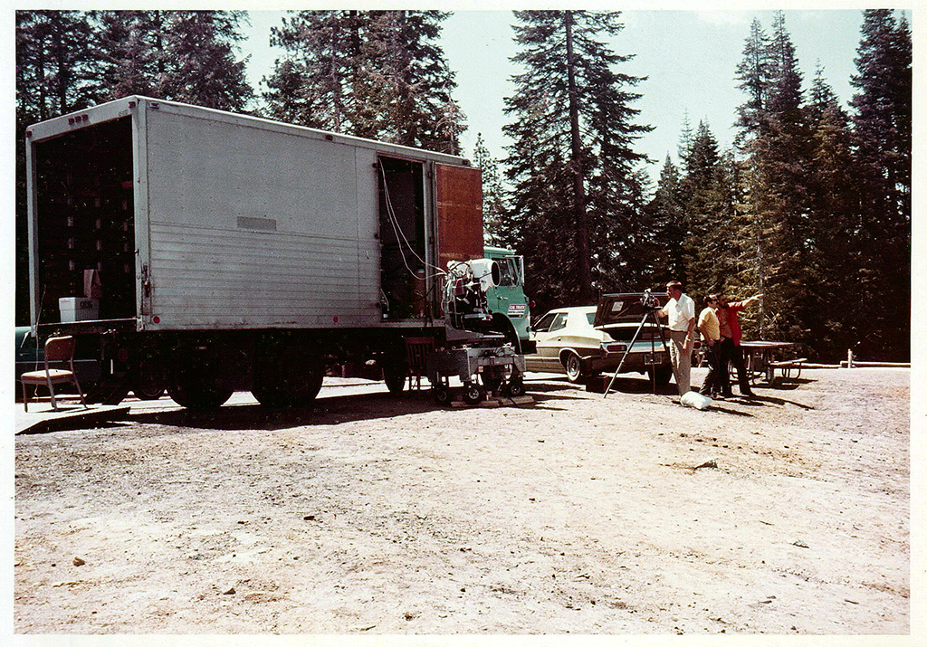 Side view of the transport truck with a side door open and the MSS on the ground in front of the door. Tall pine trees can be seen behind the truck.