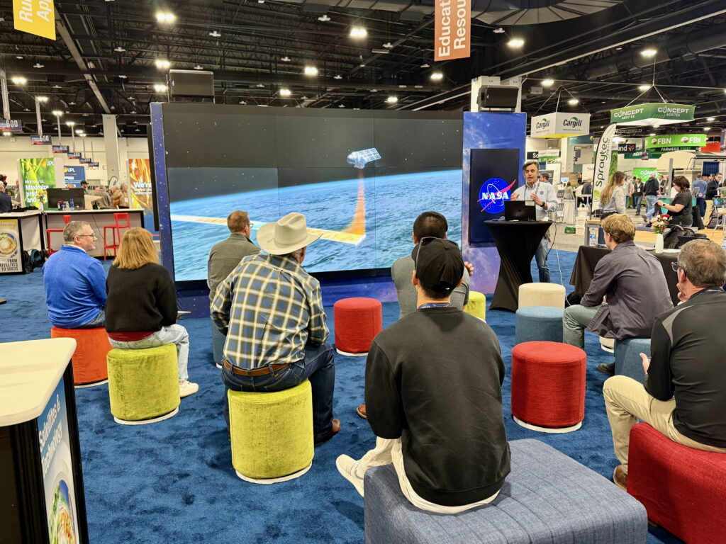 A group of conference-goers watching a speech in front of a large screen