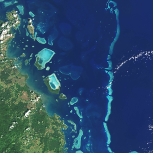 A Landsat satellite natural-color image of light blue coral peeking through the deep blue ocean.